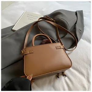 Detail view of a brown leather bucket bag with side buckle straps and a fur ball charm