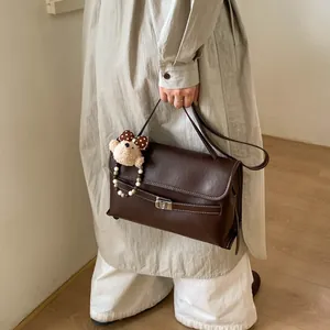 Dettaglio della borsa tote vintage in pelle marrone con cuciture bianche e ciondolo orso