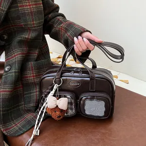Detail einer braunen glänzenden Ledertasche mit Klarsichtfach und Plüschbär-Anhänger