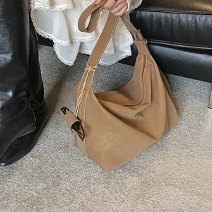 Close-up of a large camel suede bucket bag with wide shoulder strap and metal buckle detail