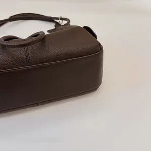 Detail of dark brown lychee grain leather tote bag with reinforced stitching and metal rings