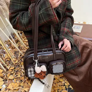 Details der dunkelbraunen glänzenden Ledertasche mit Reißverschluss und Teddy-Anhänger