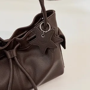 Detail of dark brown lychee leather bucket bag with drawstring and star charm pendant