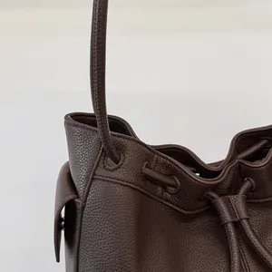 Detail of drawstring closure and pebbled leather texture on dark brown bucket bag