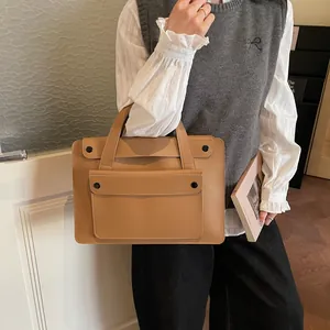 Detail view of a camel matte leather business tote held by a model in casual attire