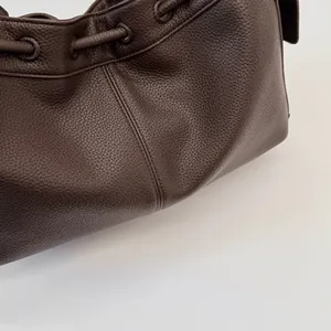 Detail of dark brown lychee grain leather texture and drawstring closure on a tote bag