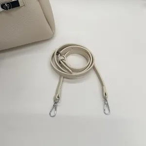 Close-up of litchi grain leather texture and silver turn-lock hardware on beige bucket bag
