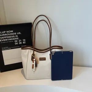 Detail of cream tote bag with contrast brown straps and decorative wooden bead tassel