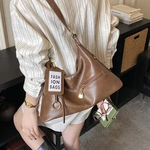 Detail of a vintage brown crossbody tote bag featuring a front zipper pocket and luggage tag