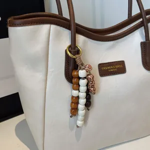 Detail of cream and brown tote bag featuring leather label and beaded charm accessory