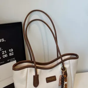 Detail of a large white tote bag with brown leather trim and a beaded tassel charm
