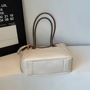 Detail of a large cream tote bag with brown straps and wooden bead decorative charms