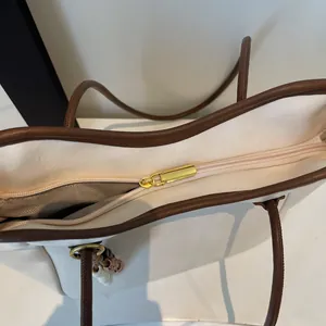 Detail of the top zipper closure on the off-white tote bag with contrasting brown straps