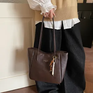 Detail of dark brown leather tote bag with stylish wooden bead tassel and logo plate