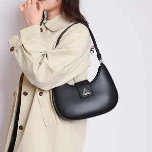 Fashionable black crescent hobo bag with triangle metal buckle worn with a beige trench coat