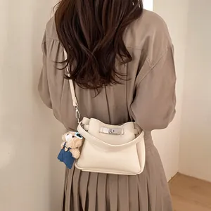 Detail of off-white lychee grain leather bucket bag featuring silver twist lock and bear charm