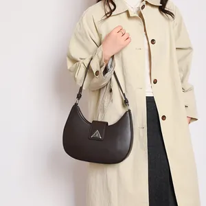 Detail of dark brown leather crescent bag with silver triangle buckle on a beige trench coat