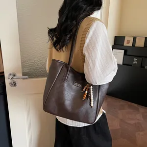 Detail of vintage brown leather tote bag with colorful wooden bead tassel and fashion logo