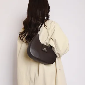 Detail of dark brown leather hobo bag with a silver triangle buckle worn over the shoulder