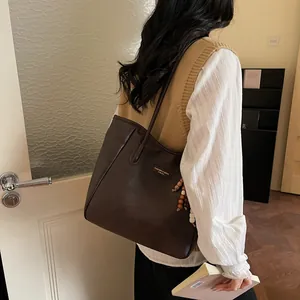 Detail of dark brown tote bag featuring beaded tassel and metal logo on matte leather