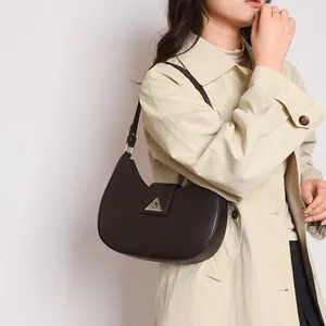 Detail of dark brown crescent shoulder bag with silver triangular metal buckle on beige coat