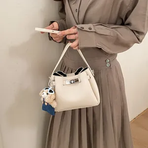 Detail of cream leather bucket bag with silver metal lock and cute teddy bear charm