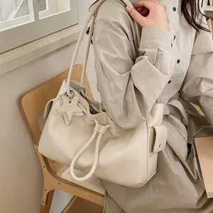 Detail of cream white leather bucket bag with star charm and drawstring closure on a wooden seat