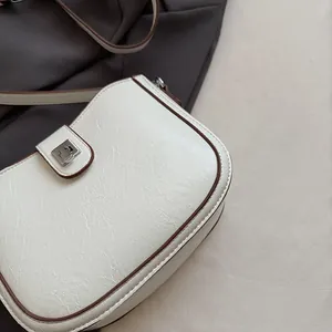 Macro detail of white saddle bag with brown trim and silver buckle on neutral background