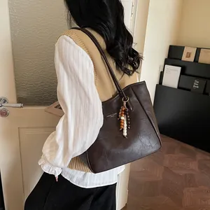 Detail of dark brown tote bag featuring retro wooden bead pendant and metal logo plate