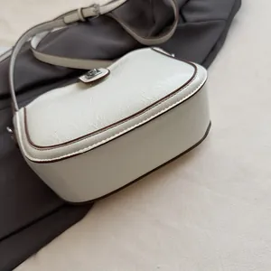 Detail of off-white saddle bag with dark brown edges and textured faux leather finish