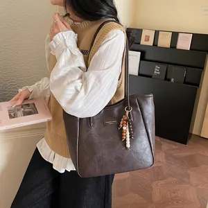 Detailed close-up of dark brown faux leather tote bag with vintage texture and beaded tassel