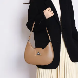 Close-up of brown leather crescent bag with silver triangular clasp worn with a black blazer