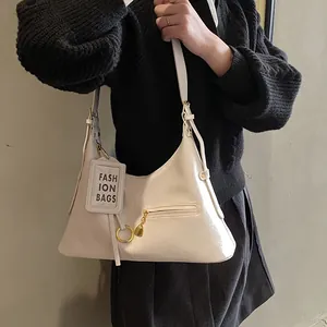 Detail view of cream white glossy leather shoulder bag with gold zipper and round pendant