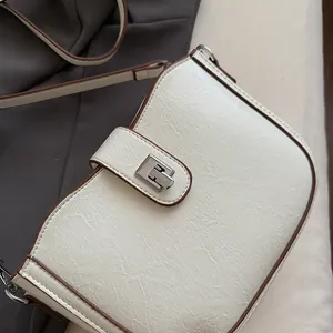 Macro detail of creamy saddle bag showing vintage crackle texture and silver clasp