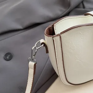 Detail of vintage cracked texture white saddle bag with silver metal hook and stitching