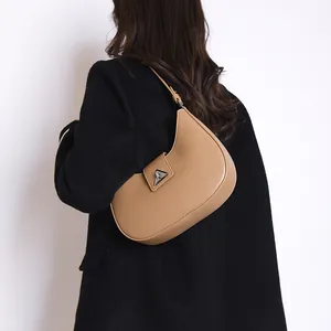 Chic light brown leather crescent shoulder bag with silver buckle worn on black coat