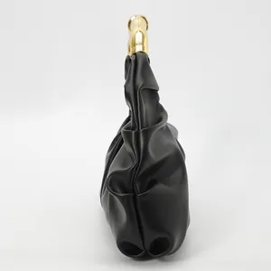 Détail d'un sac de soirée noir plissé avec une poignée métallique dorée en arc poli
