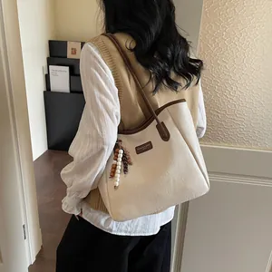Detail of a beige tote bag with brown trim and beaded pendant in a minimalist setting