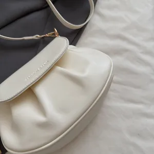 Détail du sac de selle plissé crème avec texte embossé et crochets métalliques dorés