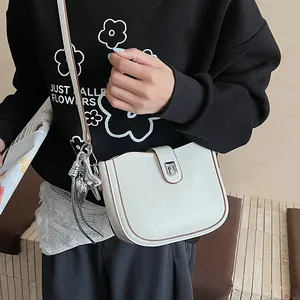 Close-up of cream saddle bag featuring vintage silver buckle and side tassel detail