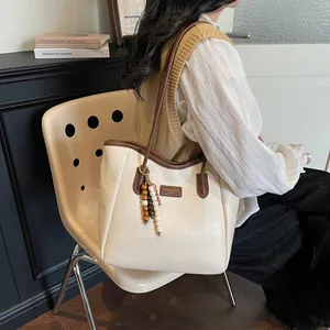 Detail view of cream tote bag with brown straps and beaded charm in a cozy setting