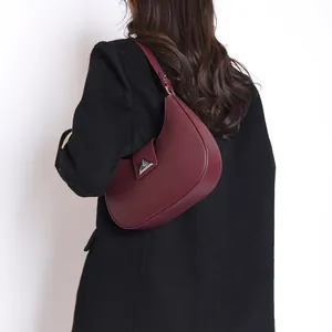 Close-up of a burgundy leather crescent hobo bag with a silver triangular buckle on model