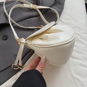 Gros plan du sac selle plissé crème avec crochets dorés sur une veste grise