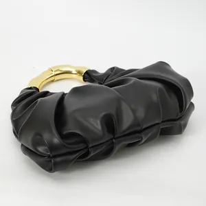 Détail de la texture plissée noire et de l'anse en anneau doré d'une pochette de soirée chic