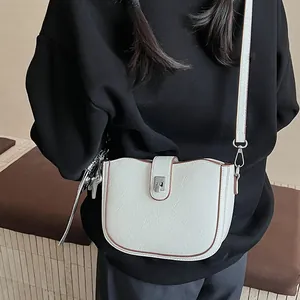 Detail of cream saddle bag with brown trim and silver heart charm on model
