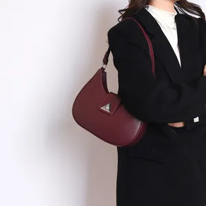 Close-up of burgundy crescent bag with matte leather and triangle metal buckle