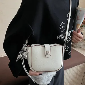 Detail of off-white saddle bag with textured leather, brown trim and silver star charm