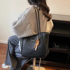 Close-up of black leather tote bag with stylish wooden bead tassel and fashion logo detail