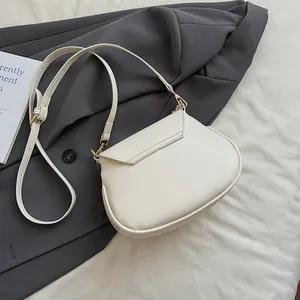 Détail d'un sac besace blanc crème avec boucles dorées sur un tissu de costume gris