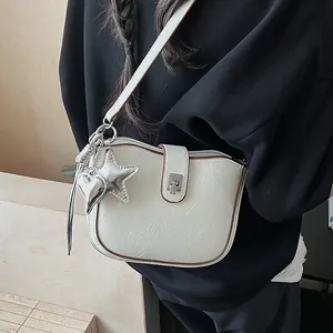 Detail of cream saddle bag with silver heart charm and turn-lock closure on model